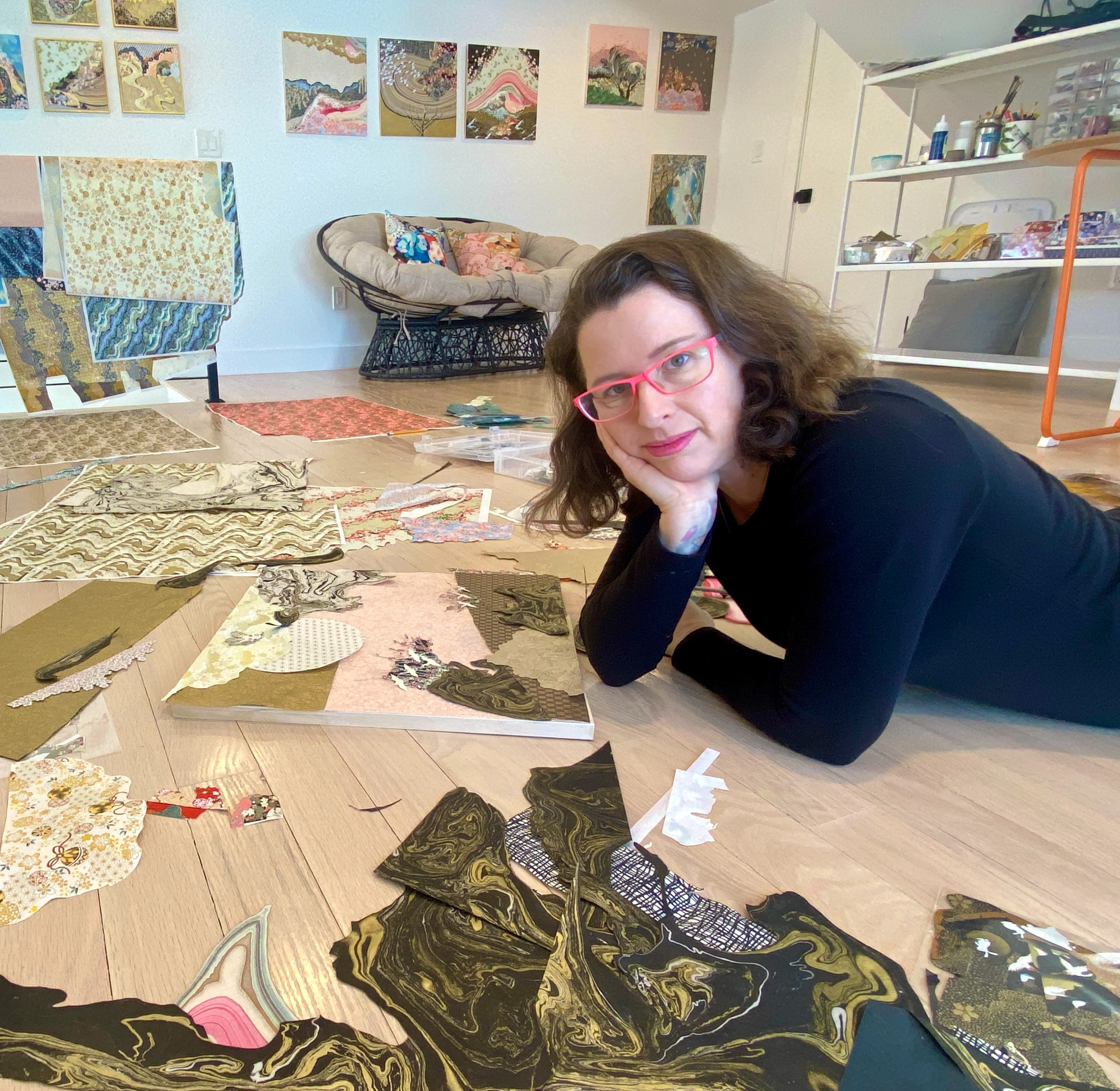 Reut wearing black and lying on the studio floor surrounded by Japanese papers and artworks in progress